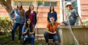 six researchers posing for a group photo, with a mist nest for capturing birds running through the middle of the group.