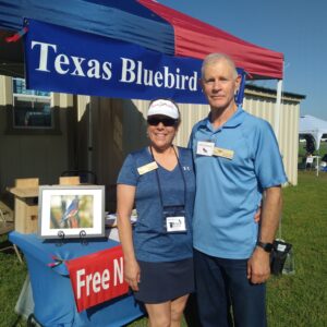 two volunteers next to an exhibit table for the Texas Bluebird Society at an outdoor festival