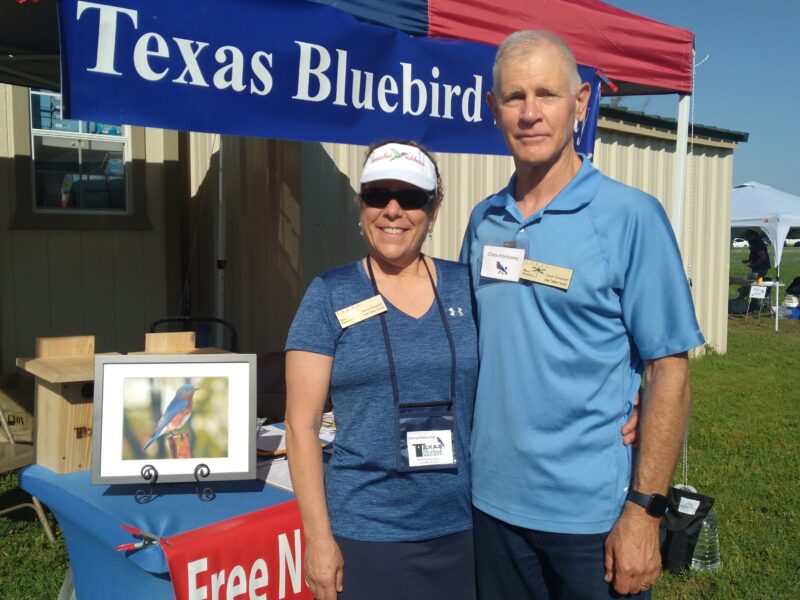 two volunteers next to an exhibit table for the Texas Bluebird Society at an outdoor festival